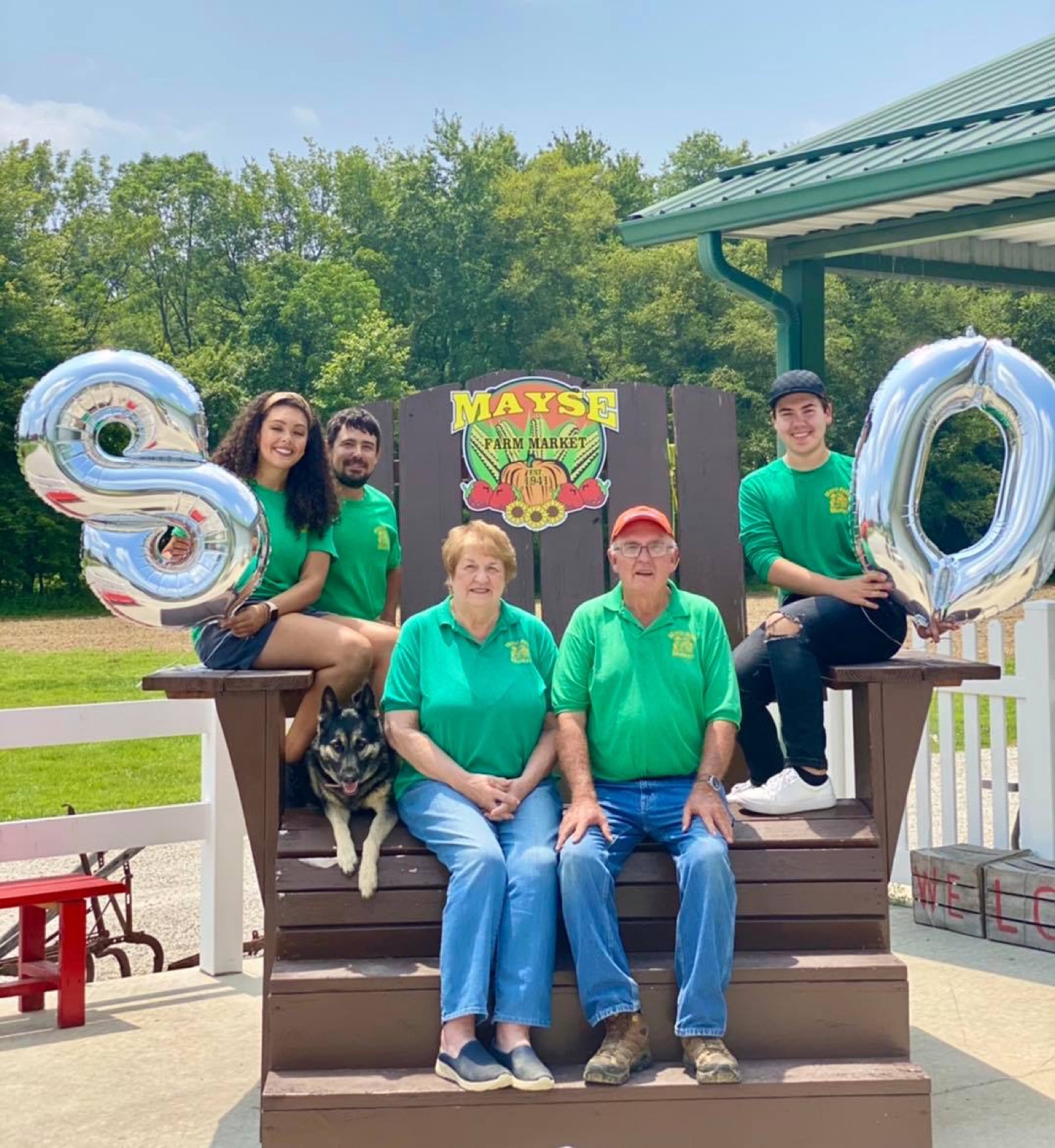 The Mayse family and Libby celebrating 80 years on the giant wooden chair, holding silver 8 and 0 balloons