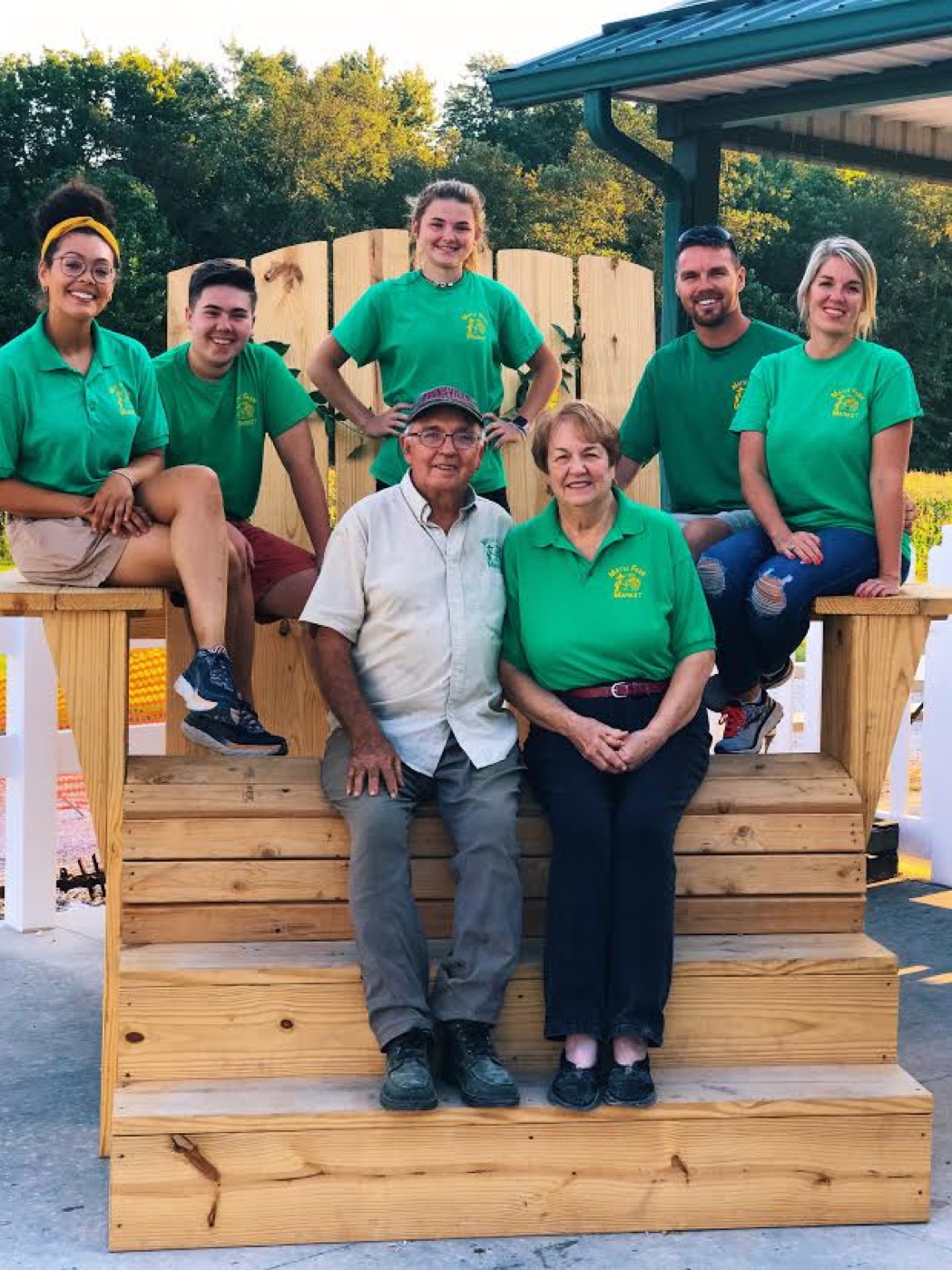 Three generations of the Mayse family posed on the oversized wooden chair in matching green shirts
